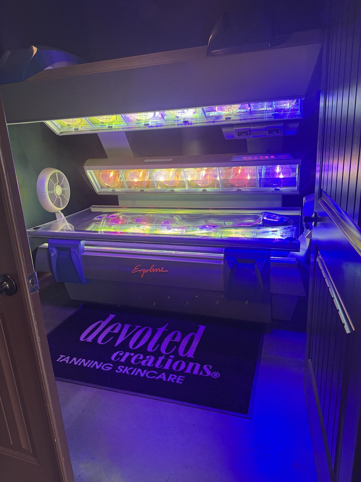 An open Ergoline tanning bed with colorful lighting inside a Sunkissd Tan tanning room